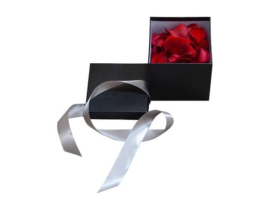A small black box with silver ribbon containing rose petals