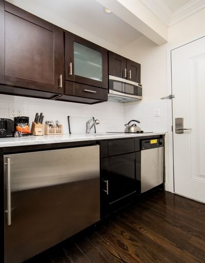 East Village Hotel room with compact kitchen with stainless steel appliances, dark cabinets, and wooden floors.