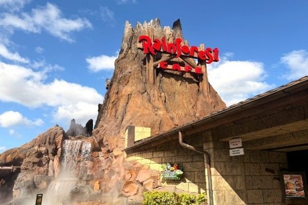 A red sign reading Rainforest Cafe on the side of a towering volcano at the entrance of the family-friendly restaurant in Orlando.