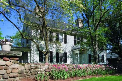Pink tulips along a stone wall in front of the Guest House behind green trees at Farmington Inn and Suites