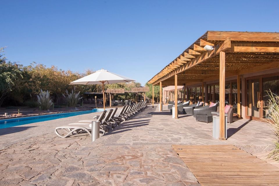 Lounge chairs and umbrellas around a pool under a wooden canopy at Hoteles Cumbres