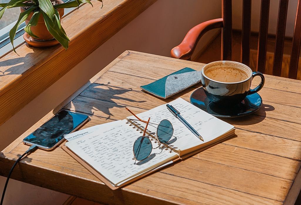 a journel, coffee drink, sunglasses, and plant on a sunny day