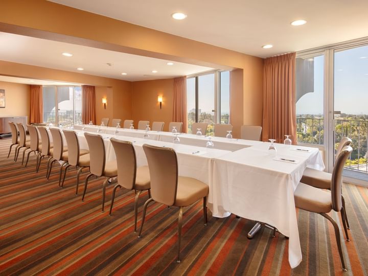 A meeting room with a long table and chairs, windows, and a city view.