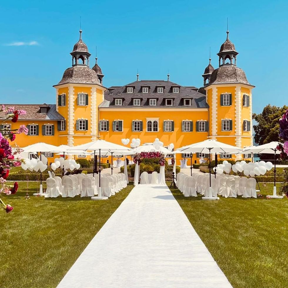 Dekorierte Hochzeitszeremonie vor einem gelben Schloss mit weißen Stühlen und Zelten