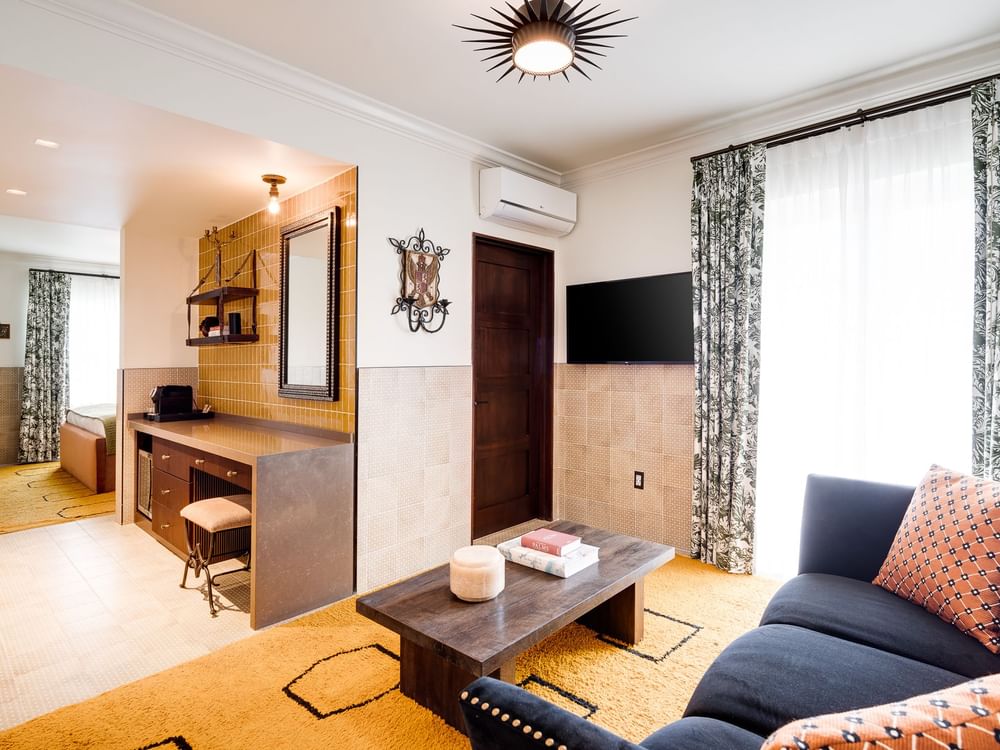 A wide view of a hotel room with a sofa, coffee table, desk, and TV.