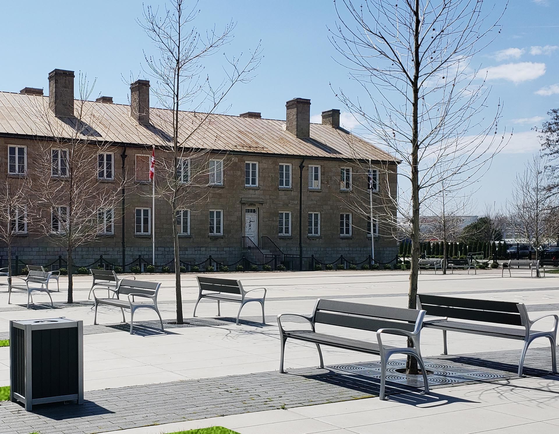 Casernes Stanley avec un mât de drapeau à l'avant et des bancs en métal sur une place pavée avec de jeunes arbres à l'hôtel X Toronto