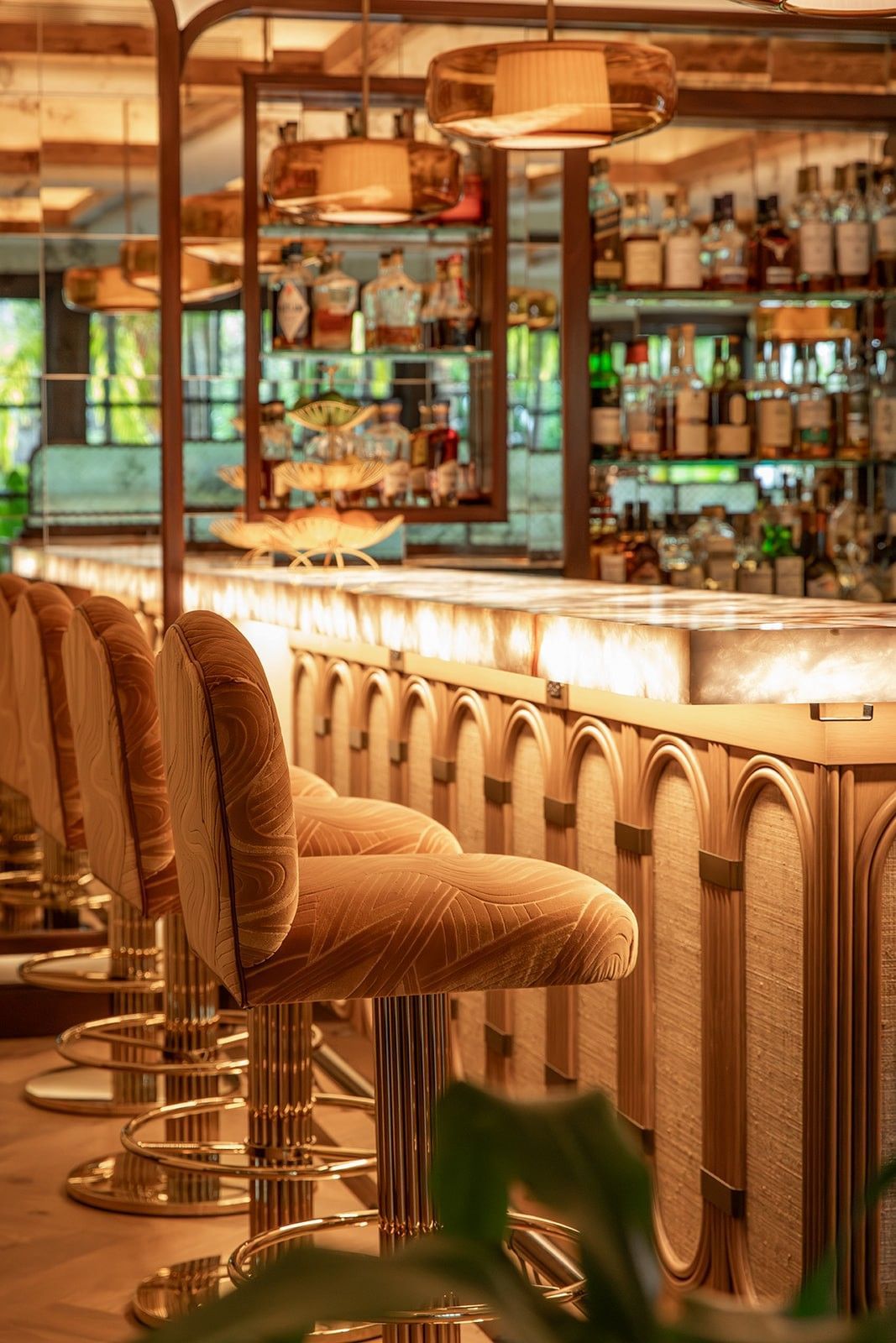 Rows of stools at a bar counter with shelves of liquor bottles and decorative items behind.
