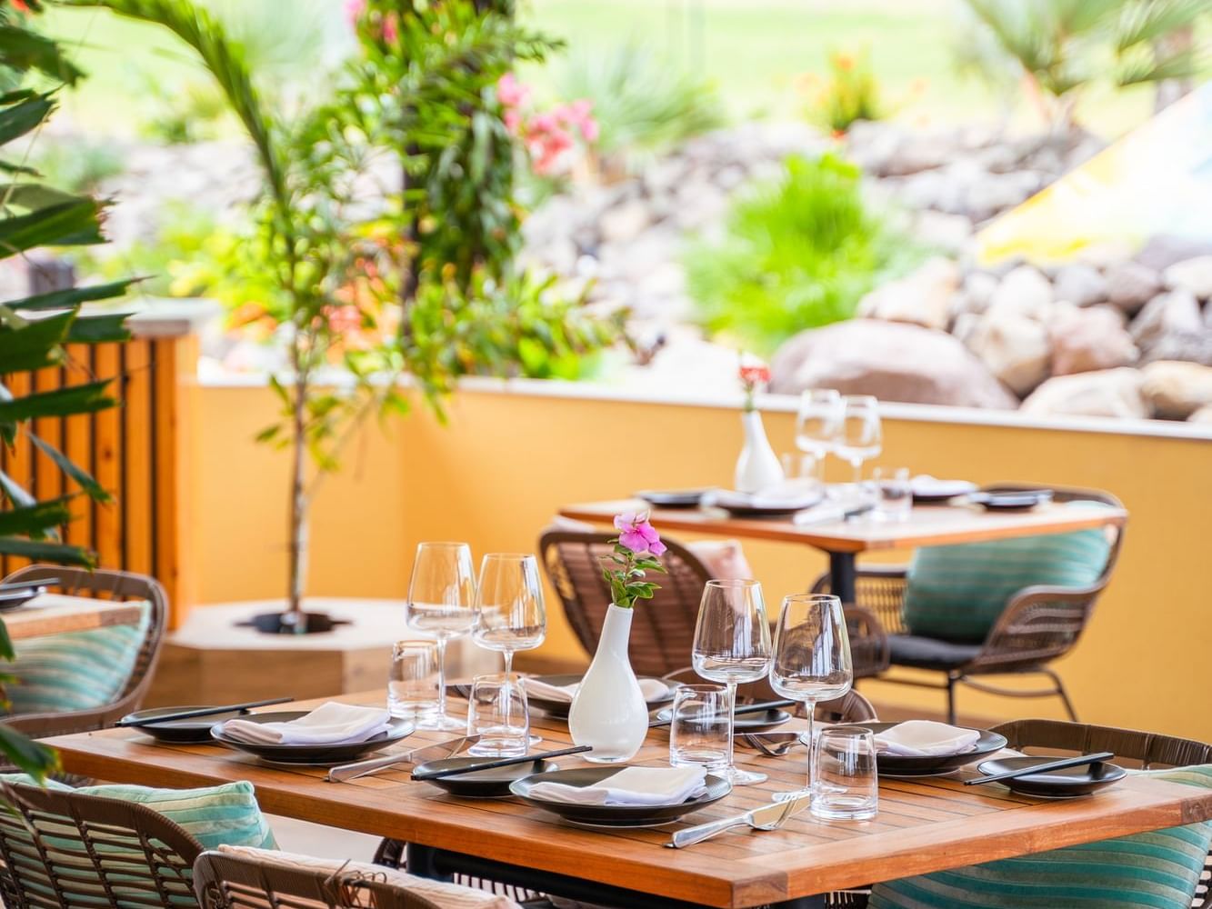 Houten tafels met glaswerk en bloemen, opgesteld voor buiten dineren in Bobbie’s Beach Club, Golden Rock Resort