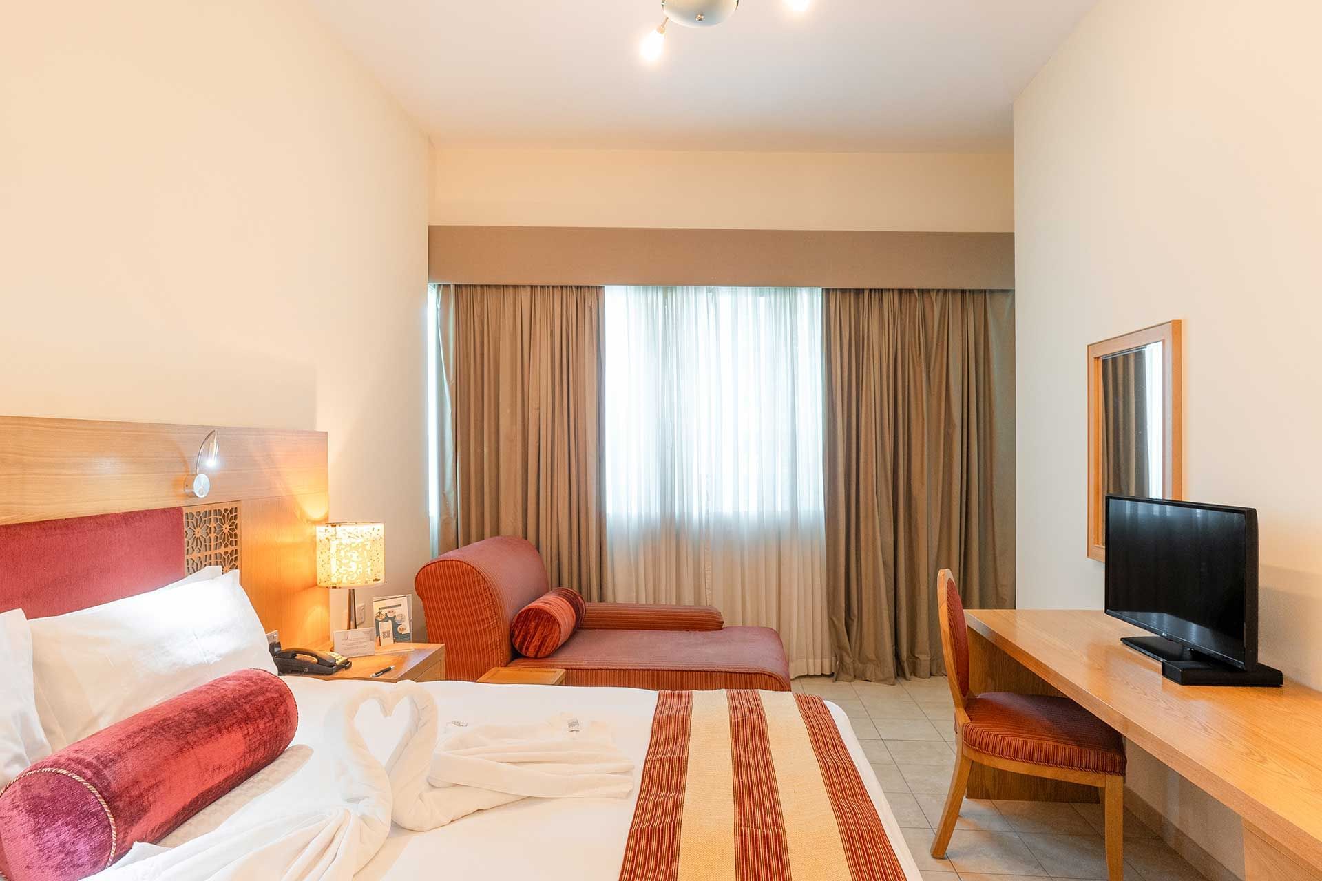 Work desk facing bed with seating by the window in a room at Tamani Marina Hotel