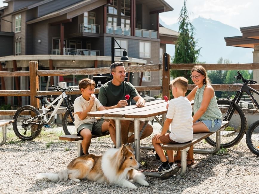 Family enjoying summer savings with bikes and dog at picnic table.