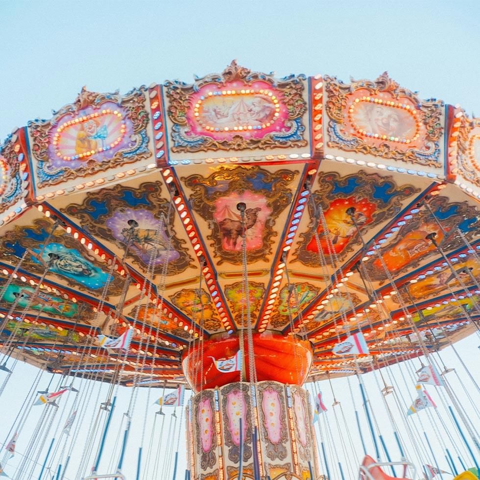 Intricately designed carousel with colorful seats and flags under a blue sky.