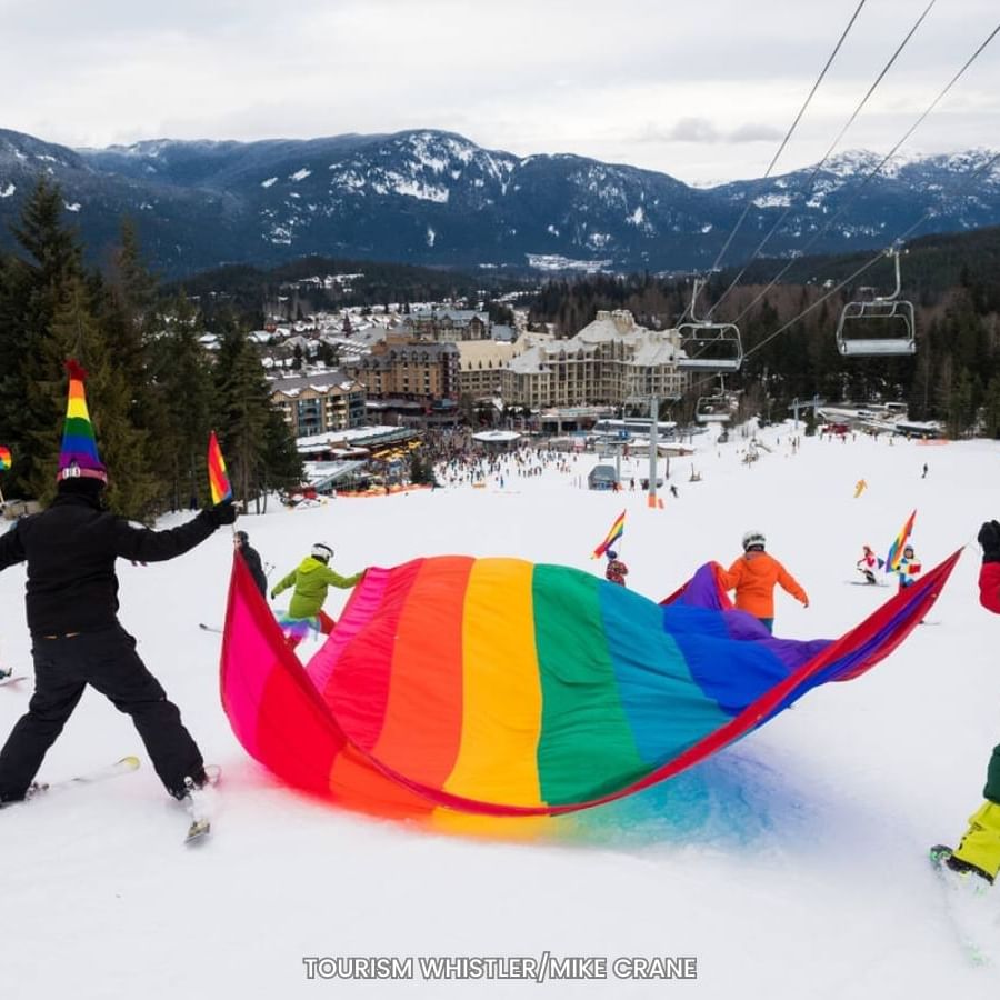 People skiing with a rainbow flag in the Whistler Pride and Ski Festival near Blackcomb Springs Suites