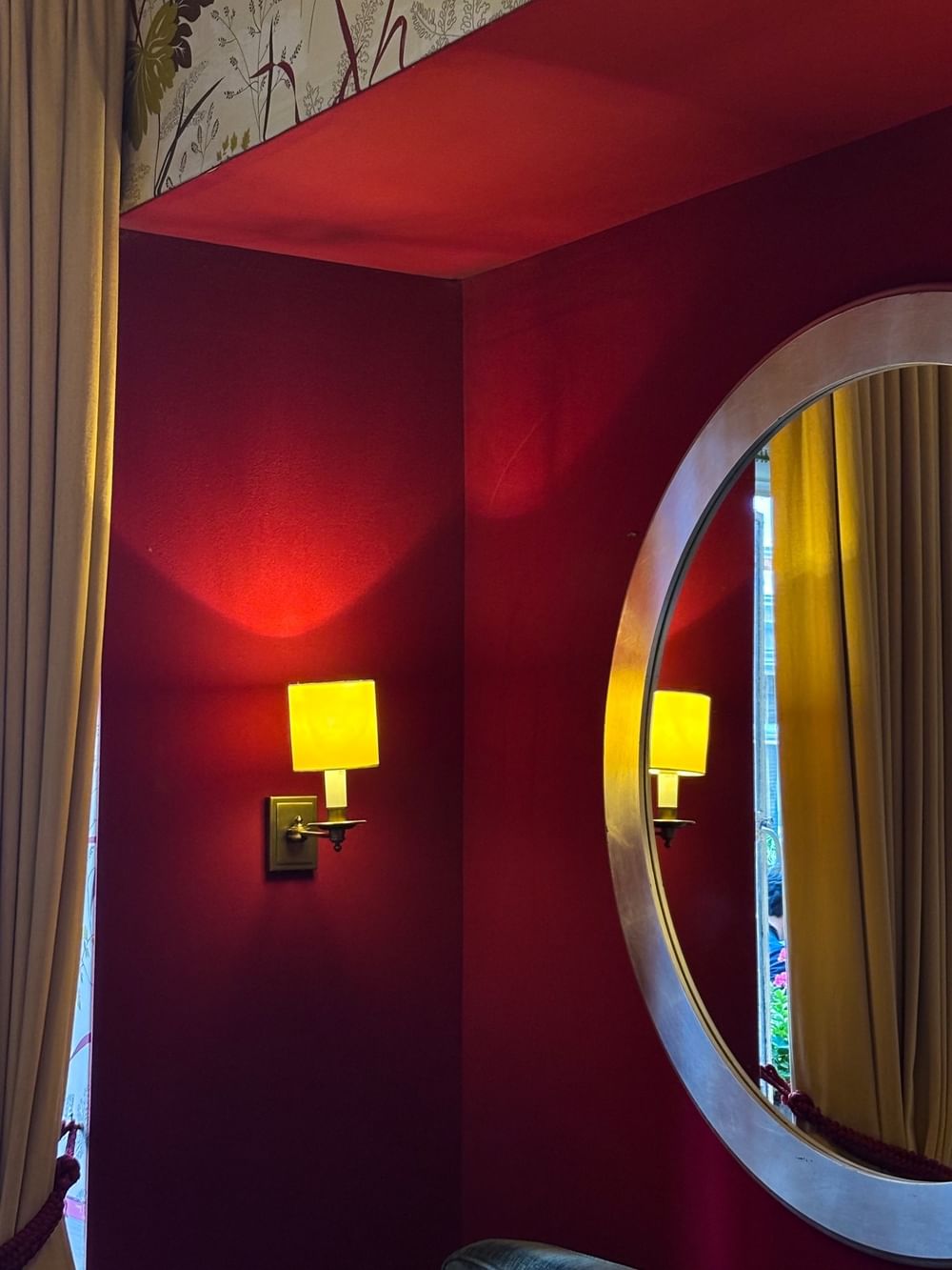 Wall lamp glowing beside a circular mirror in a red room at The Capital Hotel, Apartments and Townhouse
