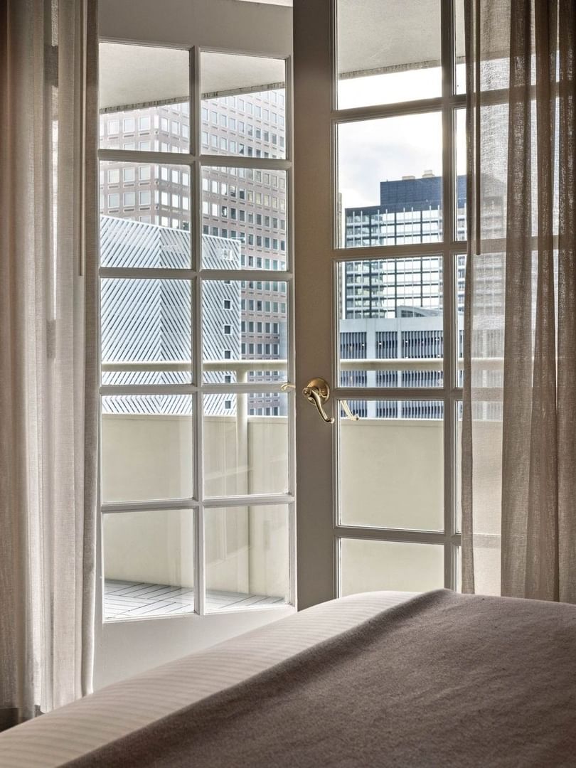 View of city buildings through a white French door with sheer curtains in Deluxe Room at Warwick Denver
