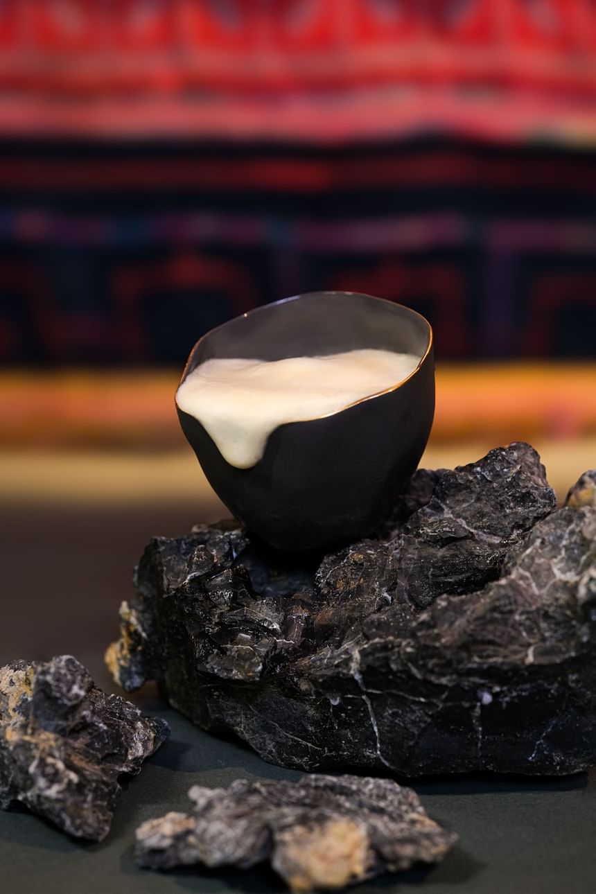 Black ceramic cup with cream spilling over sits atop dark rocks in 2 Lams Son at Park Hyatt Saigon