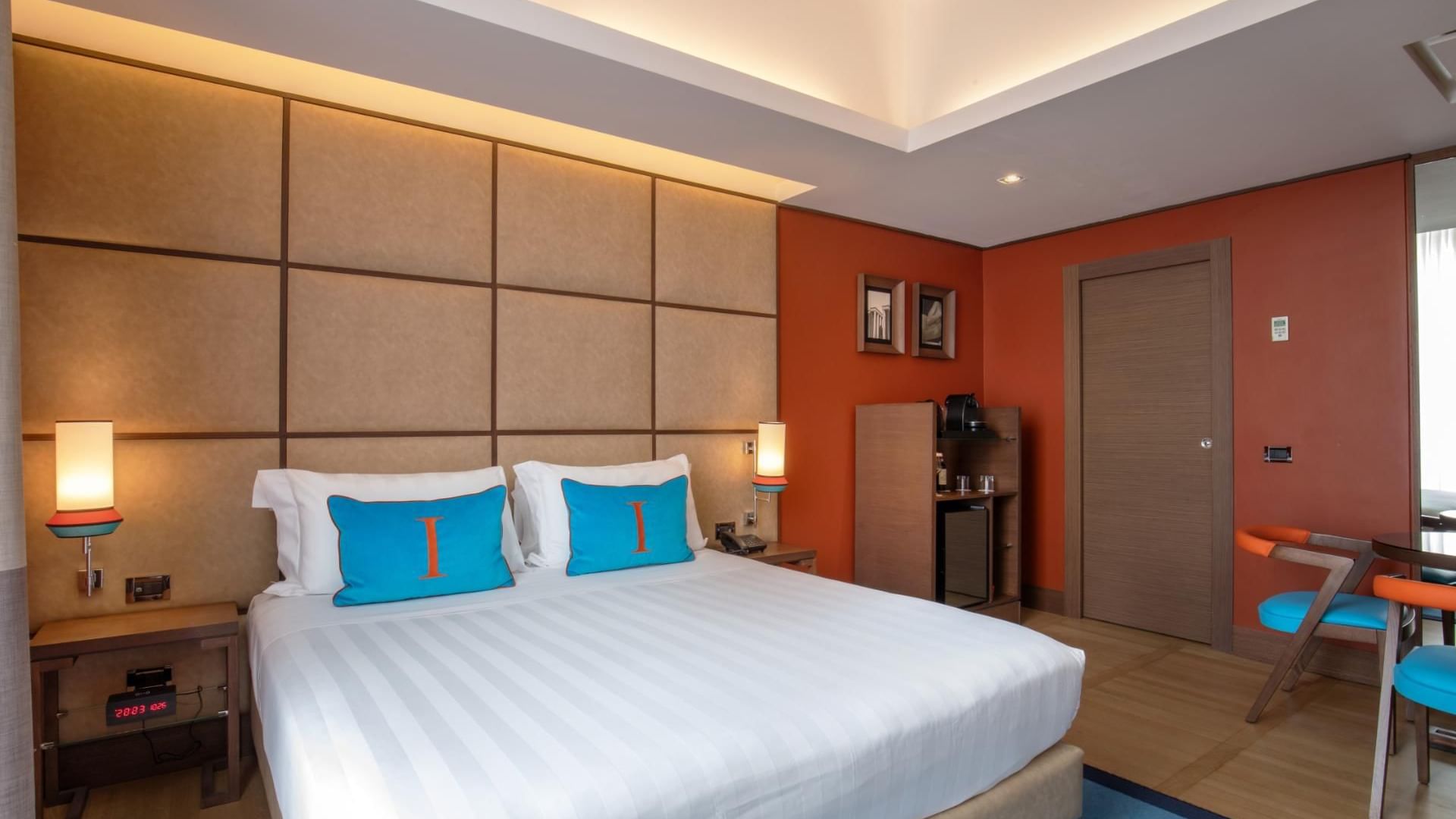 Modern Deluxe Room at The Independent with a plush bed, blue accent pillows, wooden furniture, and a coffee station