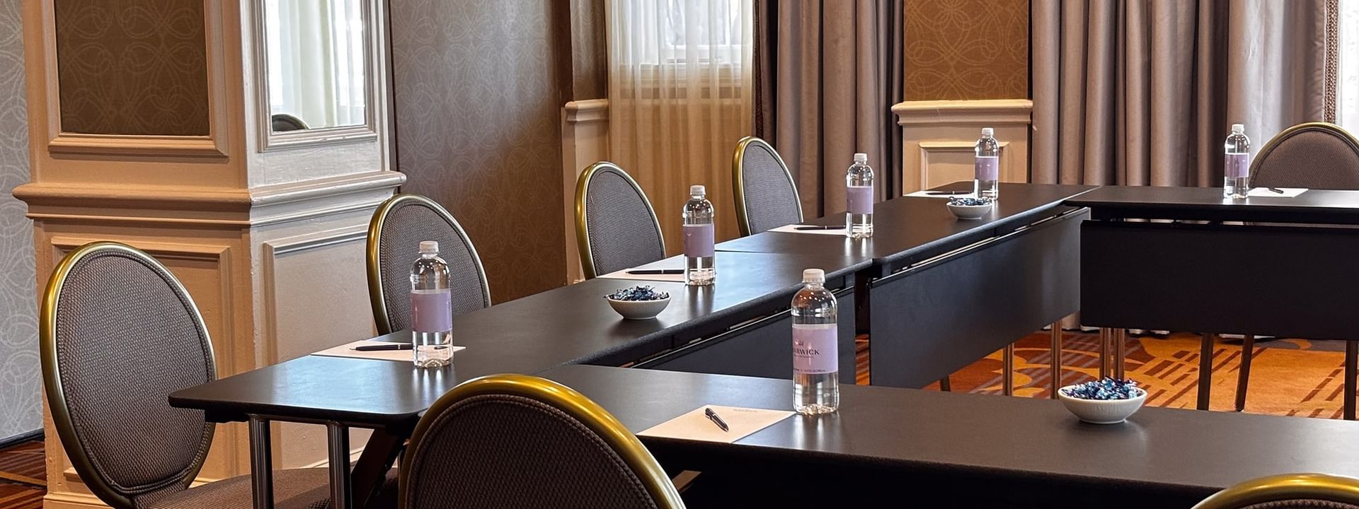 Water bottles on a black table by grey chairs under soft light in Oak Lawn/Terrace at Warwick Melrose Dallas