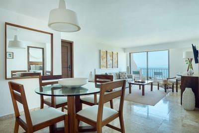 Modern living room with dining set, large mirror, couch, balcony with ocean view, and decorative elements.