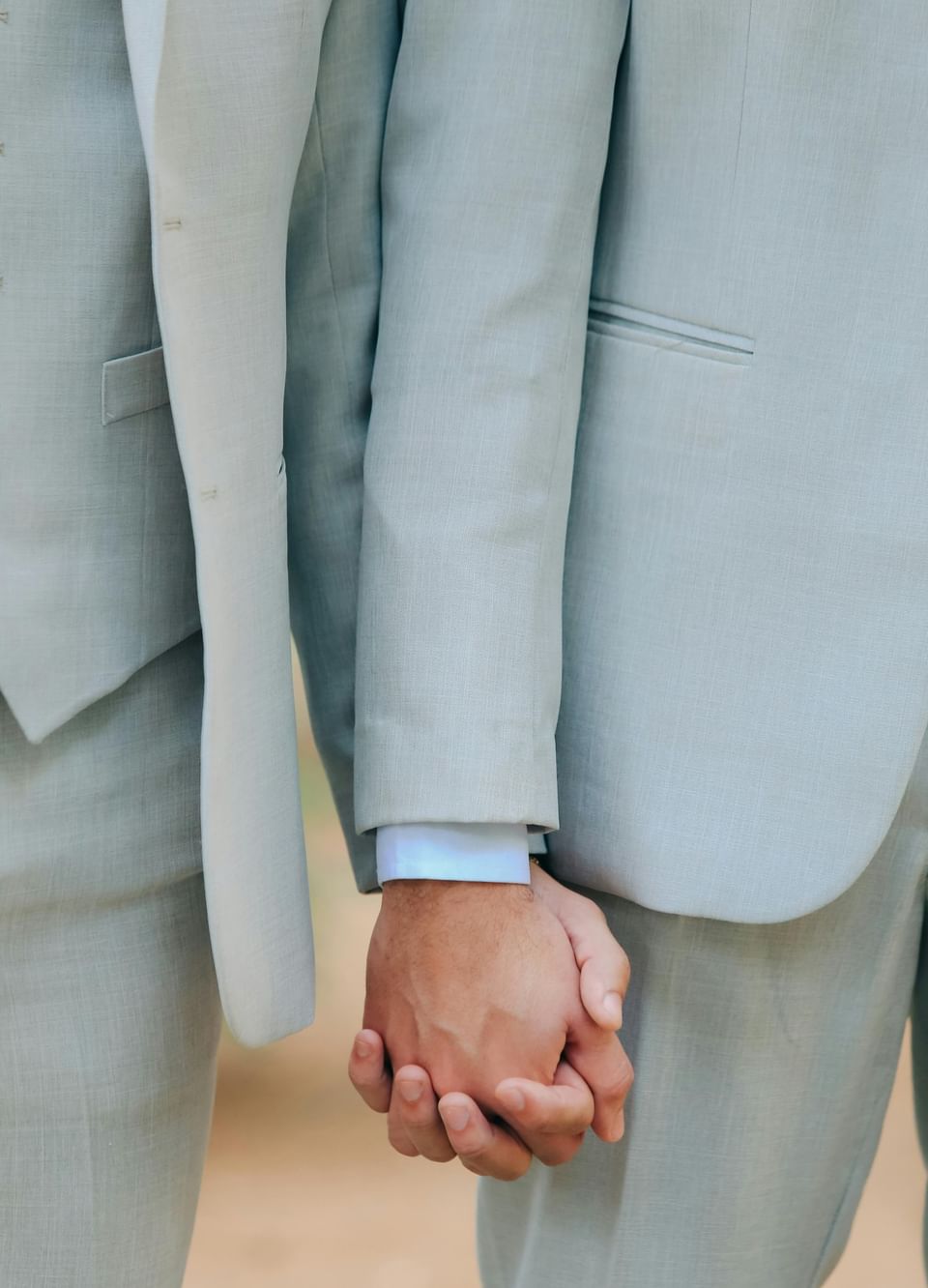 Close-up of two grooms in light suits holding hands during a ceremony at The Met Hotel Leeds, England
