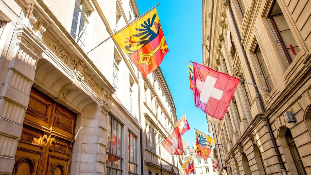 Swiss and regional flags by historic buildings under a clear blue sky near Warwick Geneva