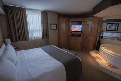 Business Suite with a King bed near a wood cabinet, beside a jacuzzi on tiled steps, at Glenmore Inn & Convention Centre