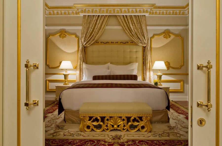Gold-carved bench by a king bed under a silk canopy and ornate gold wall panels in Royal Suite at Warwick Doha Hotel
