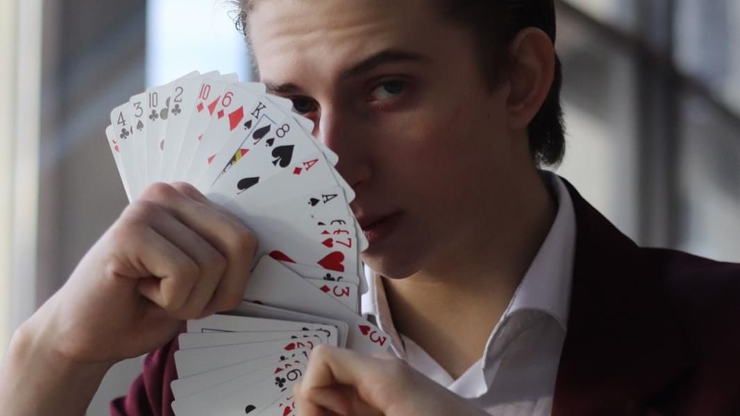 Der Magier zeigt Spielkarten in die Kamera und trägt dabei ein rotes Jackett.
