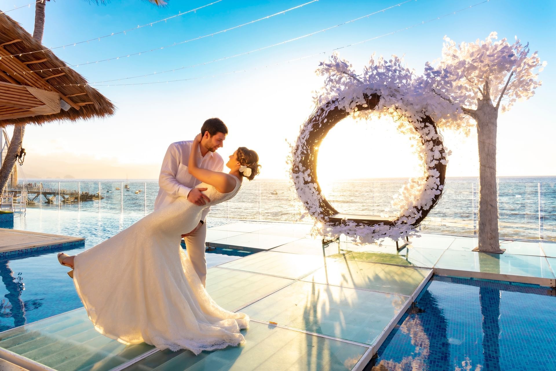 Bride and groom posing beside a large floral wreath, facing the beautiful ocean view at the Los Arcos Suites