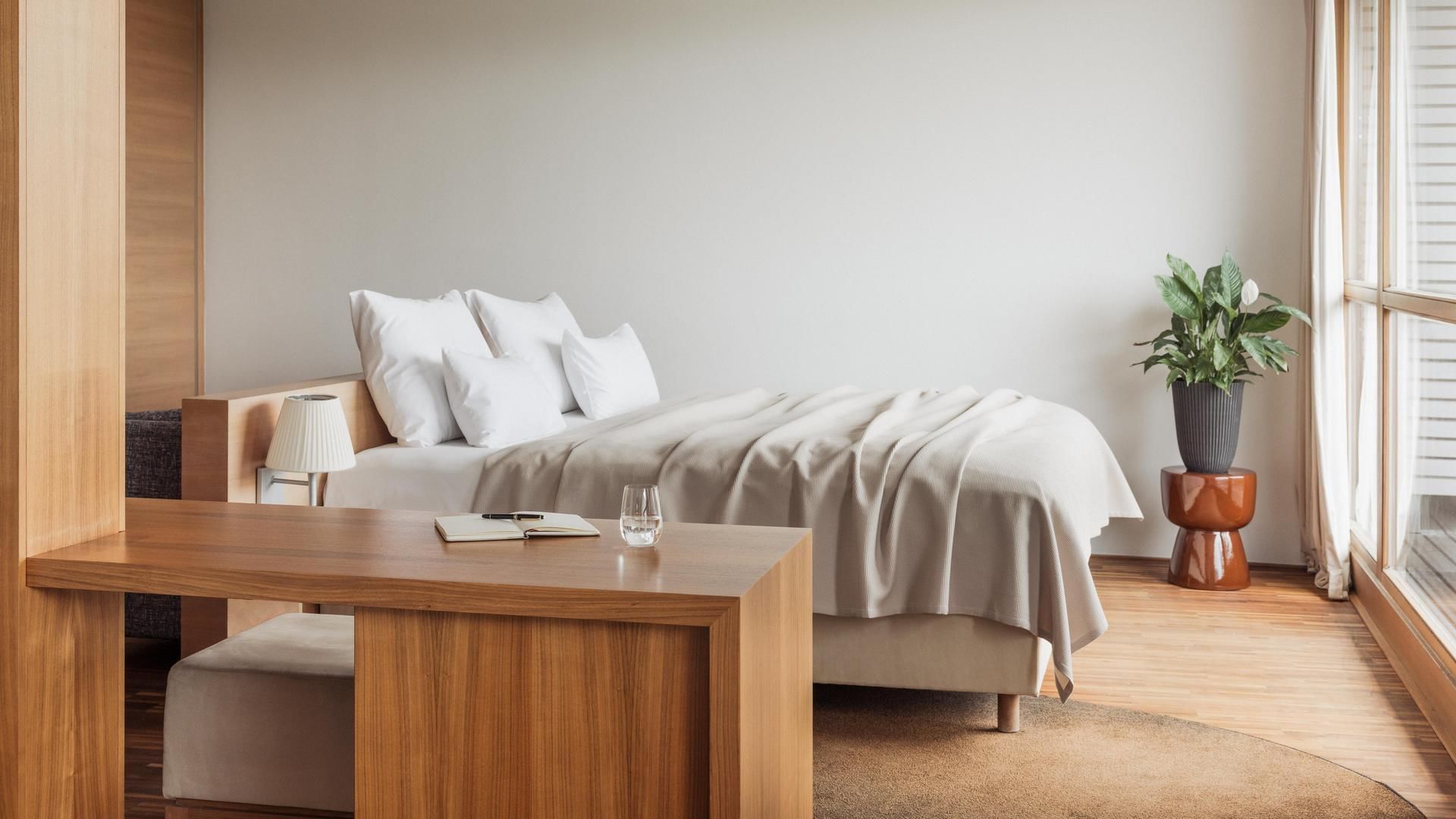 Gemütliches Schlafzimmer mit hellen Wänden, einem Bett, einer Pflanze und einem Schreibtisch.