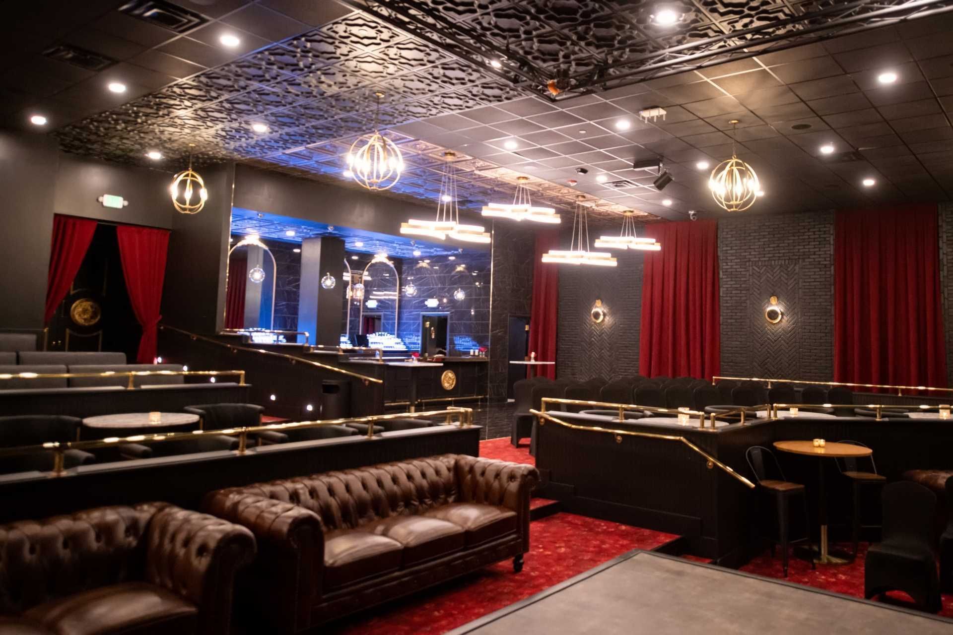 Casino lounge with leather sofas and round tables arranged by red curtains under decorative lights at The Brook