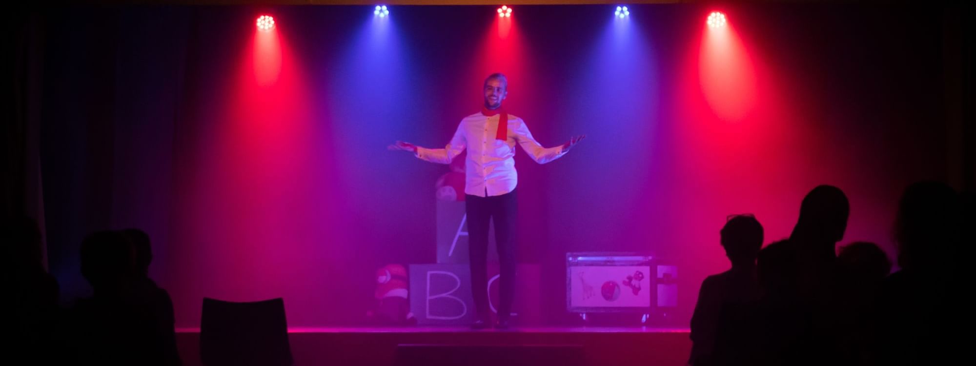 Performer in a white shirt on stage with arms outstretched under colorful lights at Novotel Sunshine Coast Resort