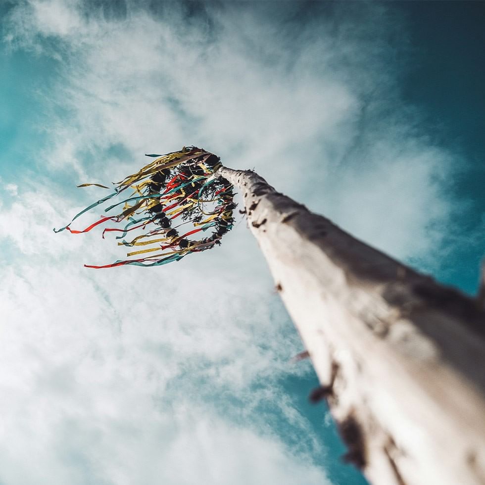 A traditional maypole cutting with colorful ribbons under a blue sky.
