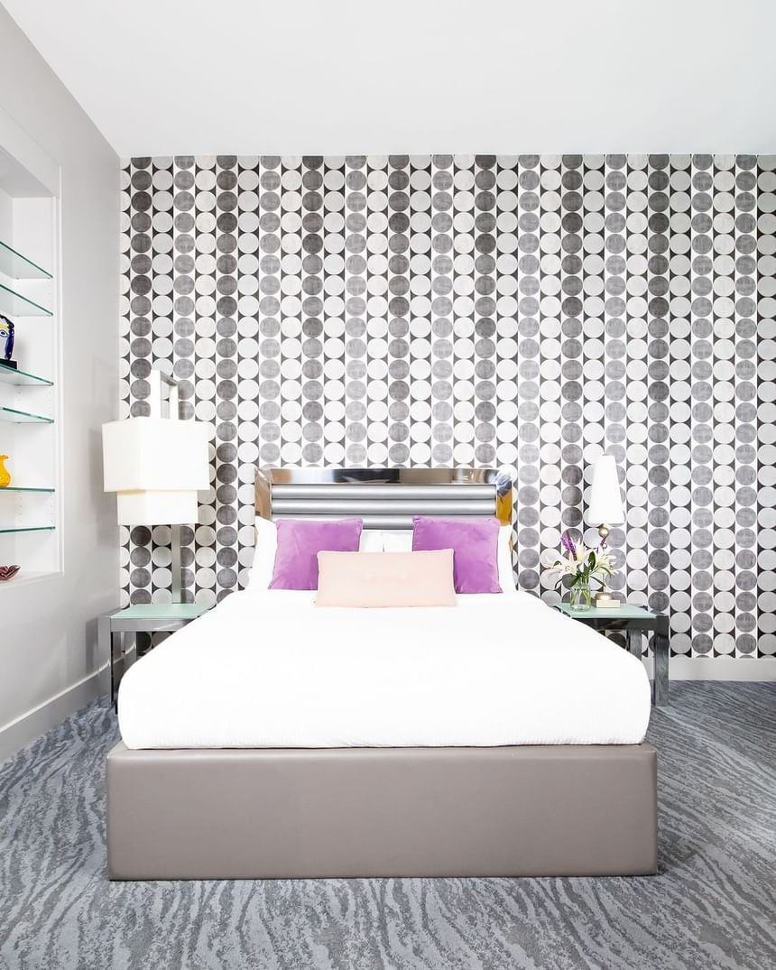 queen bed with purple accent pillows in front of decorative wall