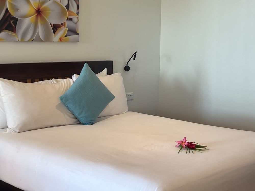 White bed with a blue pillow by a tropical flower under a floral painting at Warwick Hotels & Resorts