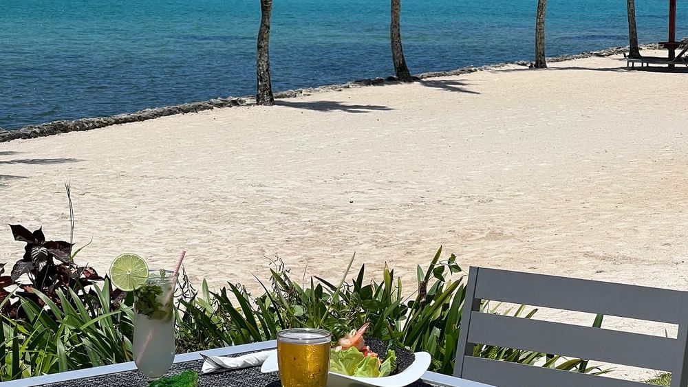 Outdoor dining table with food and drinks by the beach at Warwick Le Lagon - Vanuatu, Efate.