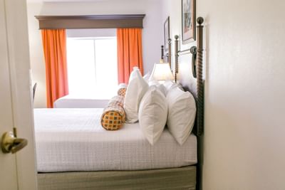 two beds with white sheets next to window and orange curtains