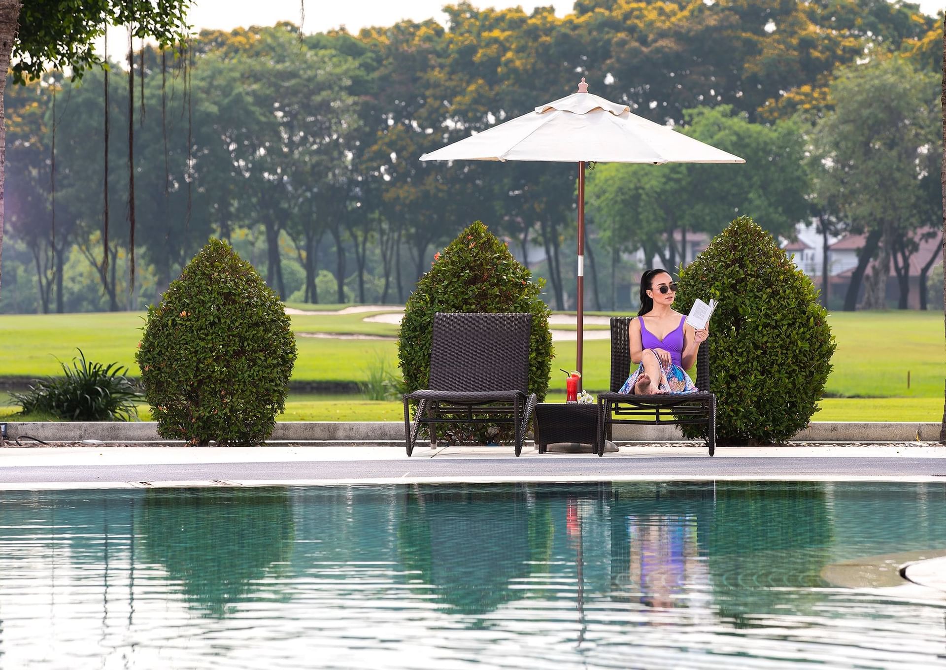 A women sitting on sunbed and reading a book near swimming pool at Eastin Thana City Golf Resort Bangkok