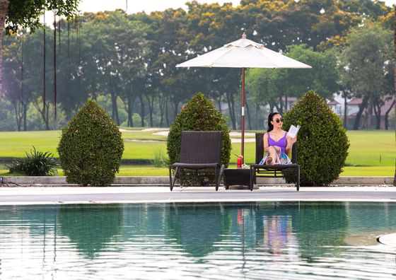 A women sitting on sunbed and reading a book near swimming pool at Eastin Thana City Golf Resort Bangkok