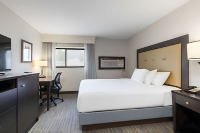 Standard King Room with white bedding, tan headboard, desk with chair, and AC window unit at Branson Hillside Hotel