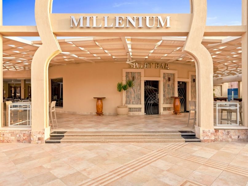 Eingang des Millennium Sportbar mit Säulen, Tischen, Stühlen und einer Pflanze in einem Topf.