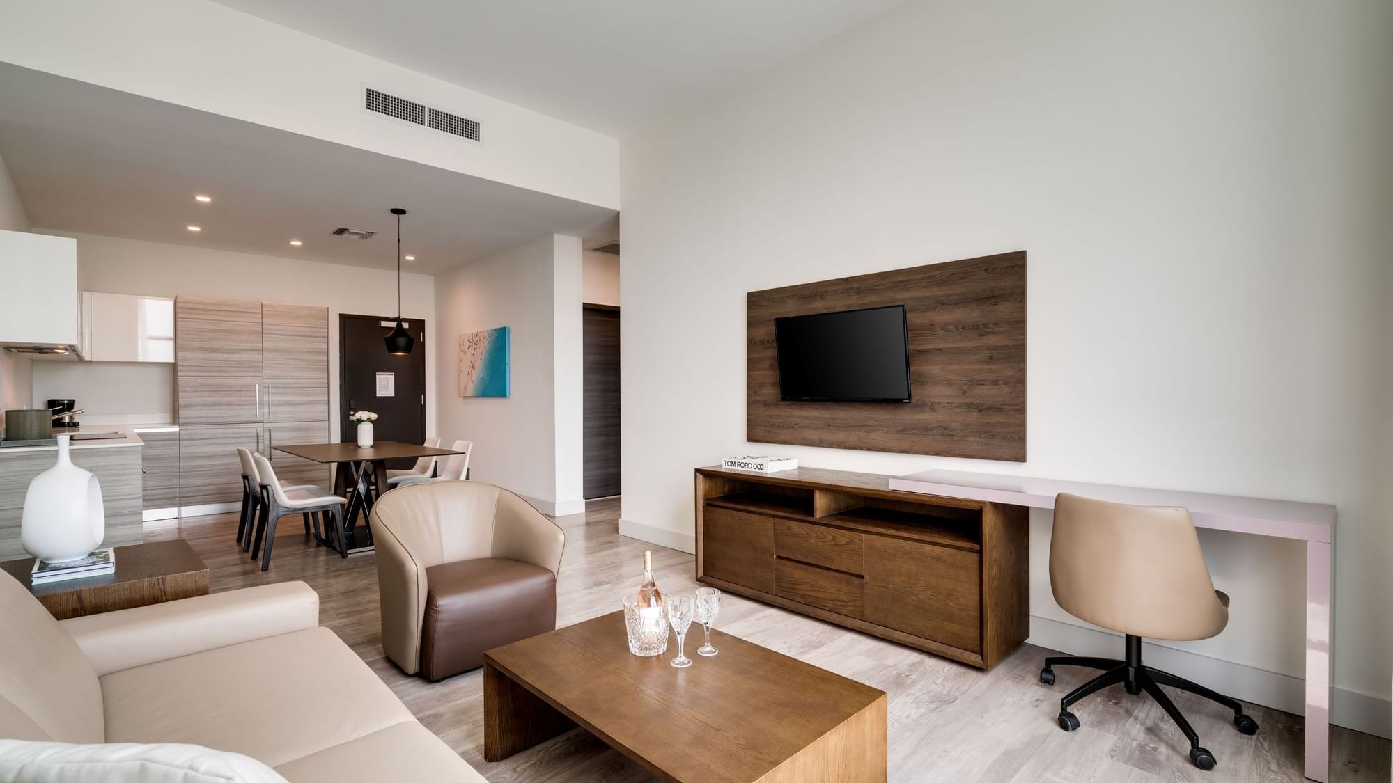 A modern living room with a kitchenette, dining area, and a TV on the wall.