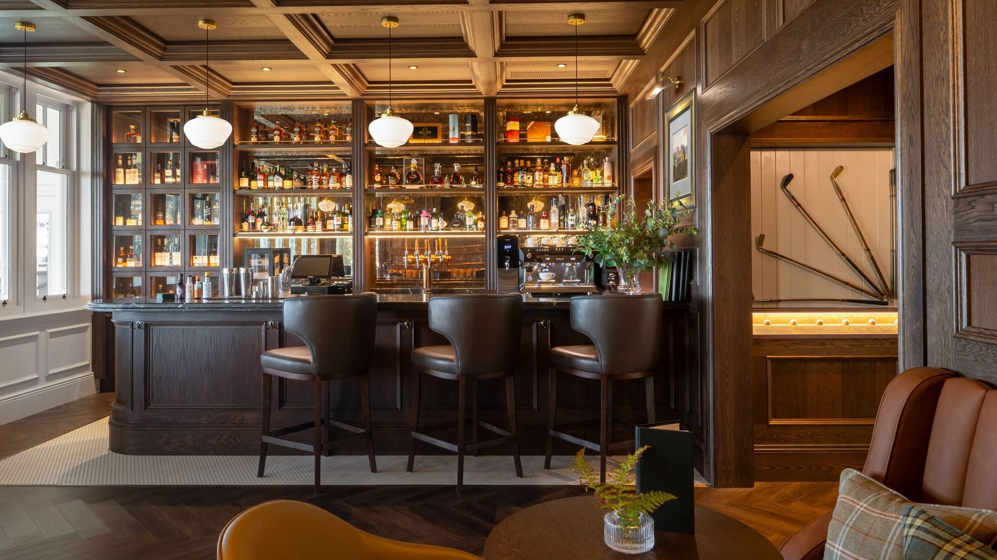 Bar with a dark wood countertop, leather bar stools, and shelves filled with a wide selection of liquor at Dunluce Lodge