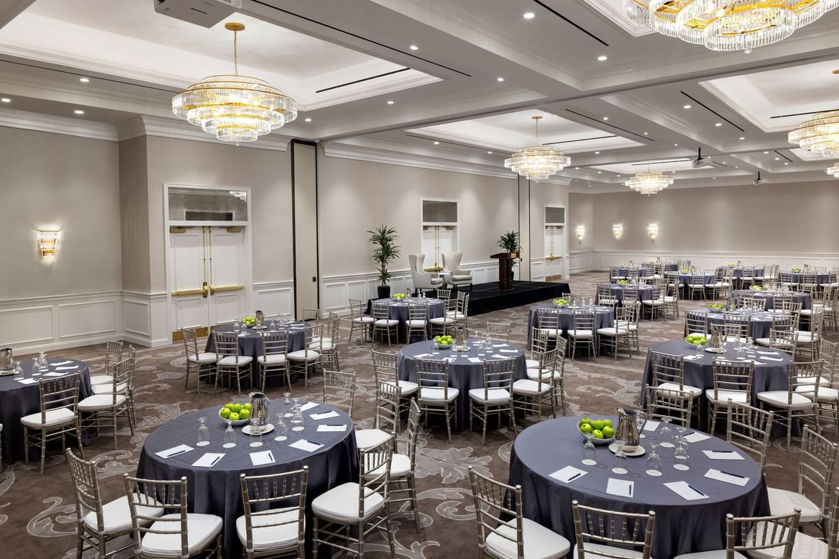 Round tables by silver chairs under crystal chandeliers in Turtle Creek Ballroom at Warwick Melrose Dallas