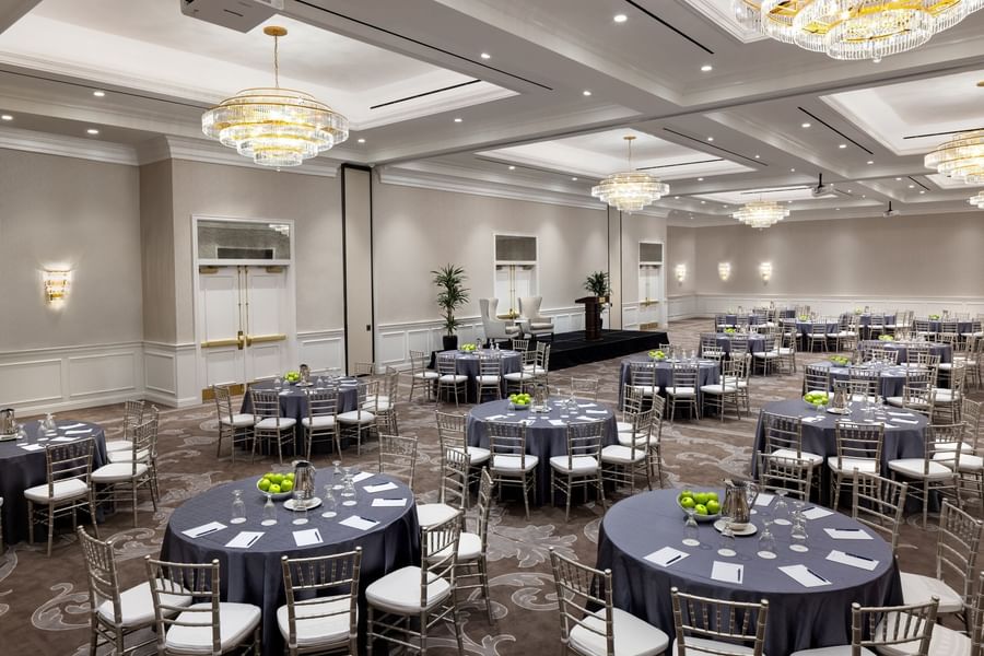 Round tables by silver chairs under crystal chandeliers in Turtle Creek Ballroom at Warwick Melrose Dallas