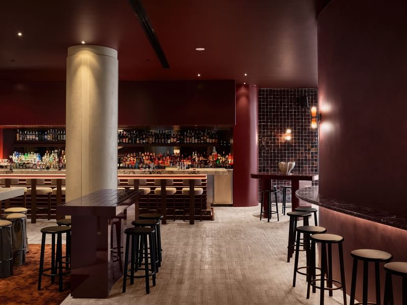 Modern bar interior with warm lighting, tall stools, sleek counter, and colorful drinks creating a stylish social setting.