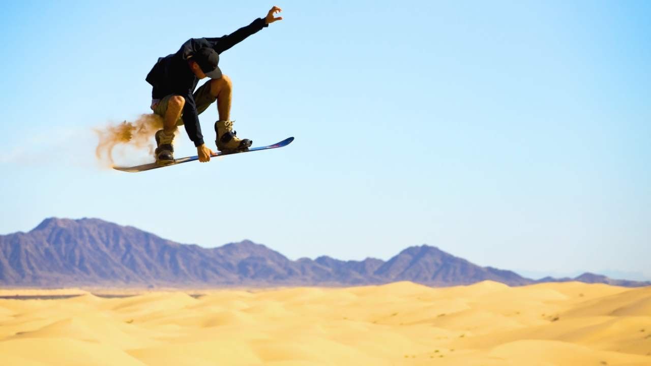 Sandboarder performing a mid-air jump over golden sand dunes and hills near Camino Real Pedregal Mexico