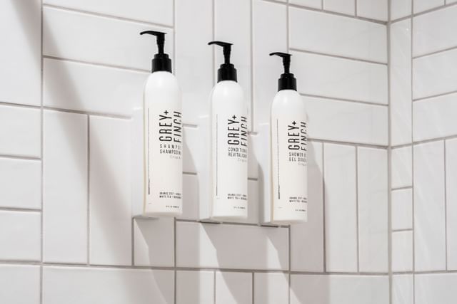 Three bottles of Grey + Finch shower products in a tiled bathroom.