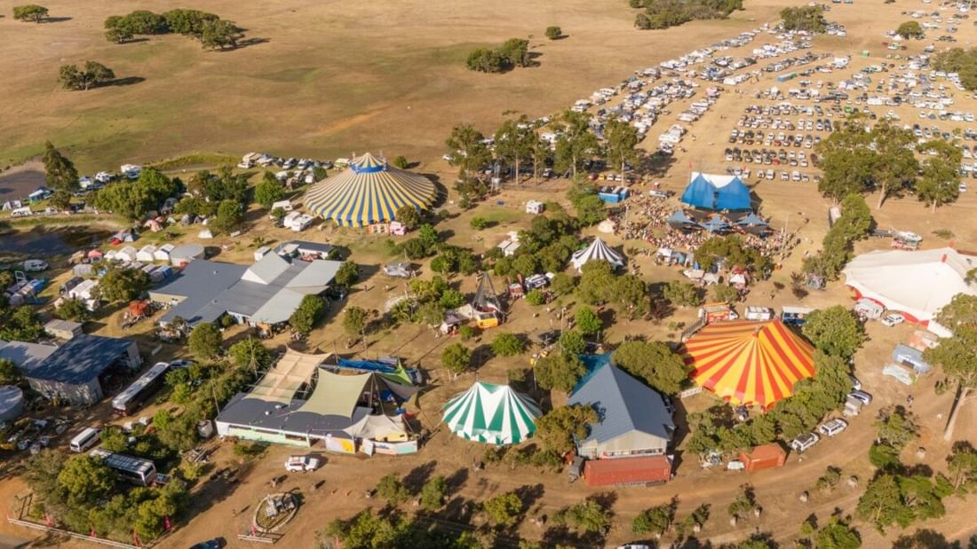 Aerial view of colorful circus tents and festival grounds surrounded by trees and open fields at Karnidale Circus Festival 2027.