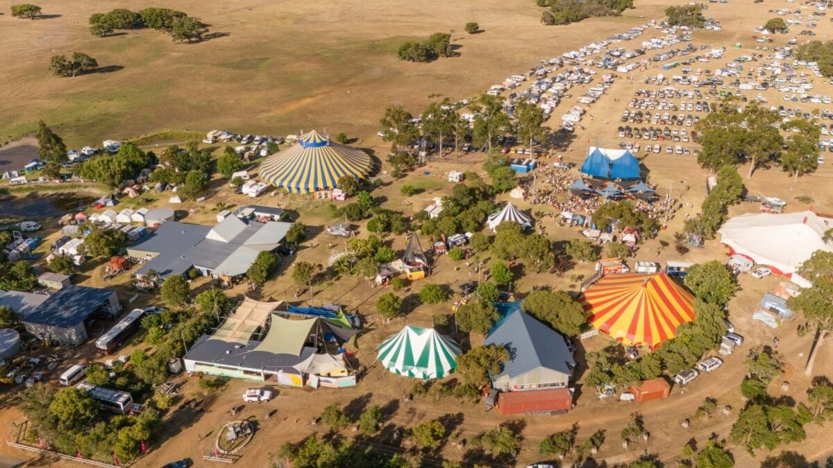 Aerial view of colorful circus tents and festival grounds surrounded by trees and open fields at Karnidale Circus Festival 2027.