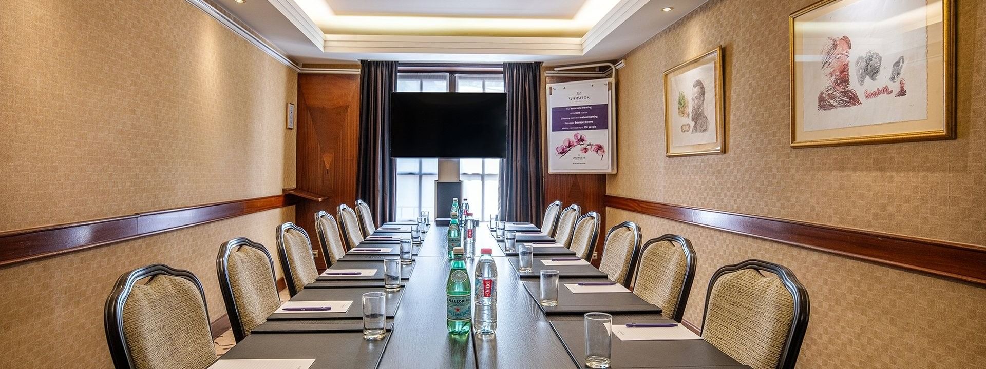 Une longue table avec des chaises, des bouteilles et des documents, dressée pour une réunion dans la salle Ensor du Warwick Grand-Place Brussels à Bruxelles.